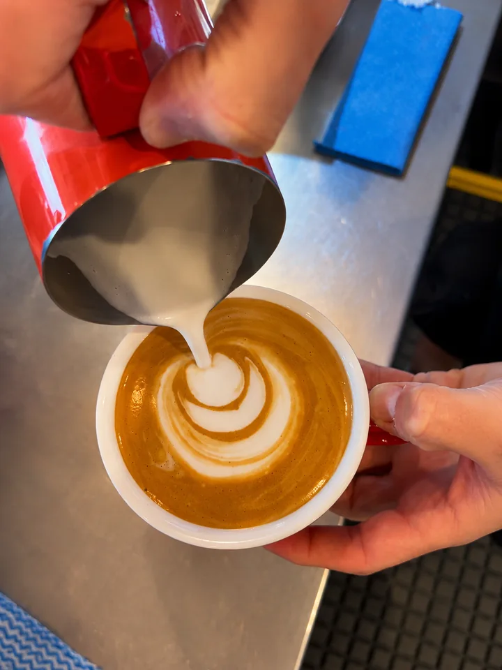 Milk being poured into a red cup to make latte art at Scarborough Fare